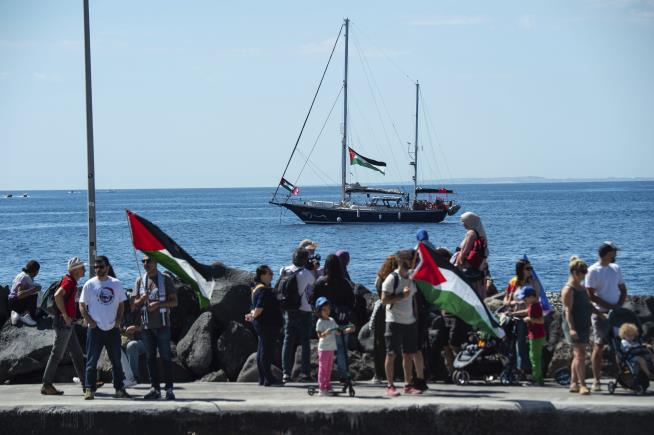 Palestine, Freedom flotilla Palestinian flags while watching a large sailboat in the sea. The boat also displays Palestinian flags and appears to be part of a pro-Palestinian flotilla. The scene takes place on 