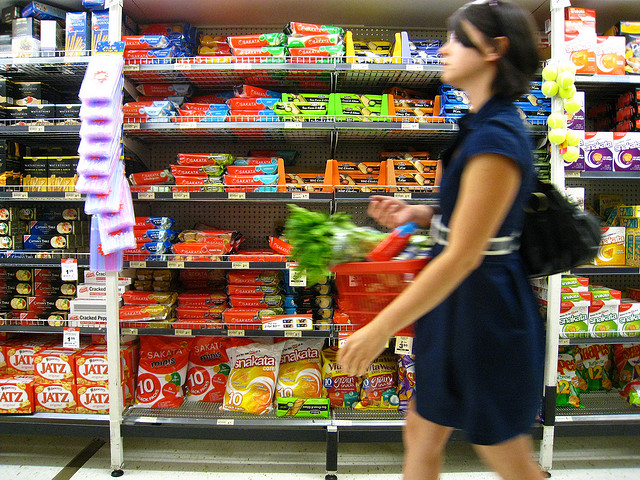 young woman purchasing greens in grocery, candy in background