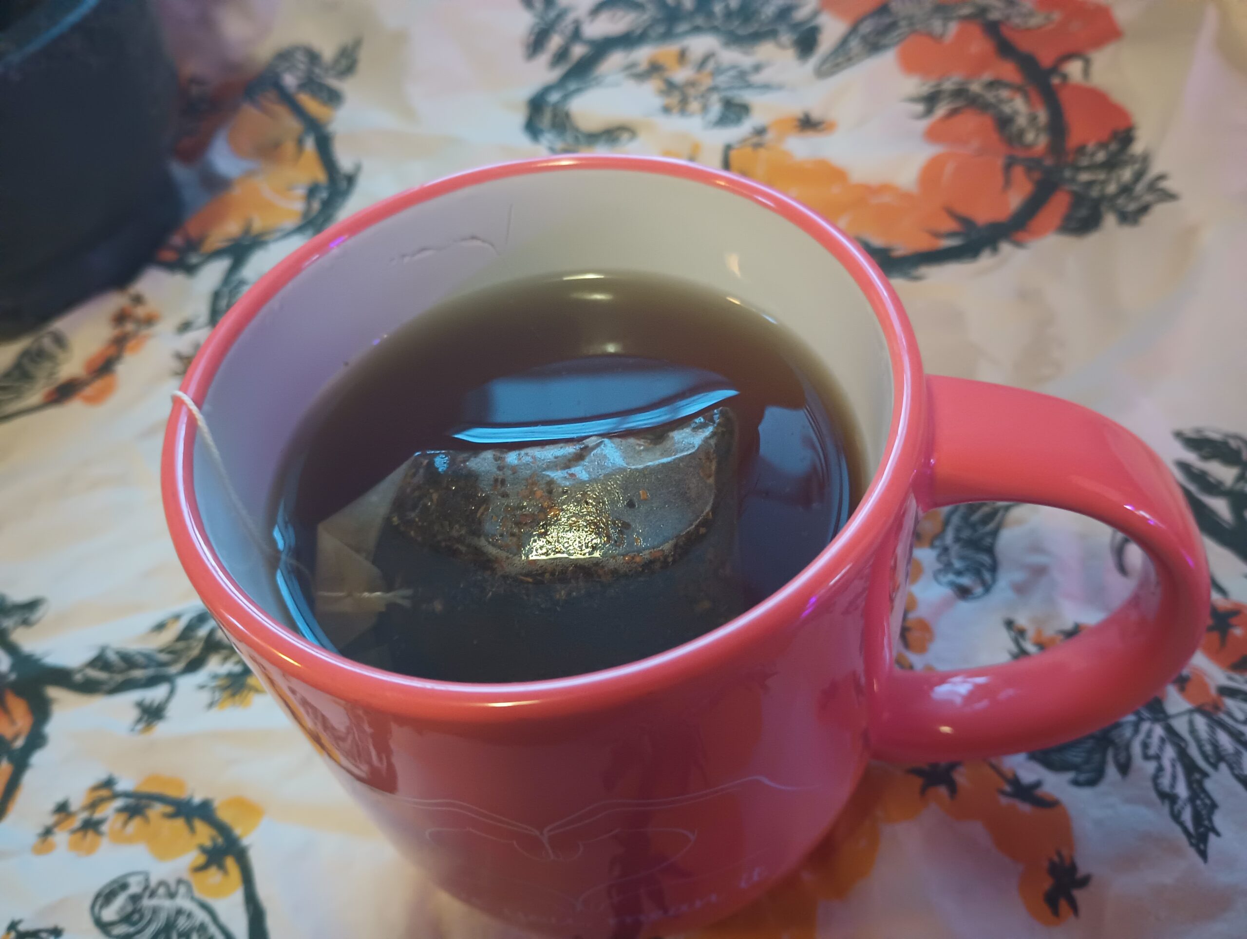 Tulsi tea in an orange tea mug sitting on a white cloth screenprinted with illustrations of hornworms crawling on tomato plants