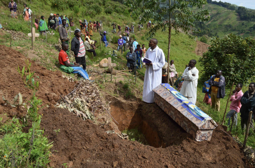Merveille Kavira Luneghe , GPJ Democratic Republic of Congo Priest Kasereka Nzandu, wearing a white robe, recites prayers while a crowd of mourners gathers at a burial site in Lubero territory.