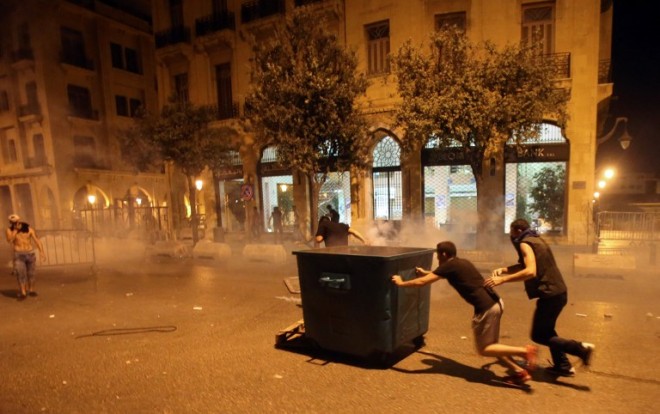 Lebanese demonstraters take shelter behind a rubbish container during clashes with security forces following a demonstration, organised by the "You Stink" campaign, against the ongoing trash crisis in the capital Beirut on August 22, 2015. Thousands of protesters, including children, gathered to protest the Lebanese government's inability to find a lasting solution to the country's worsening waste problem. AFP PHOTO / STR