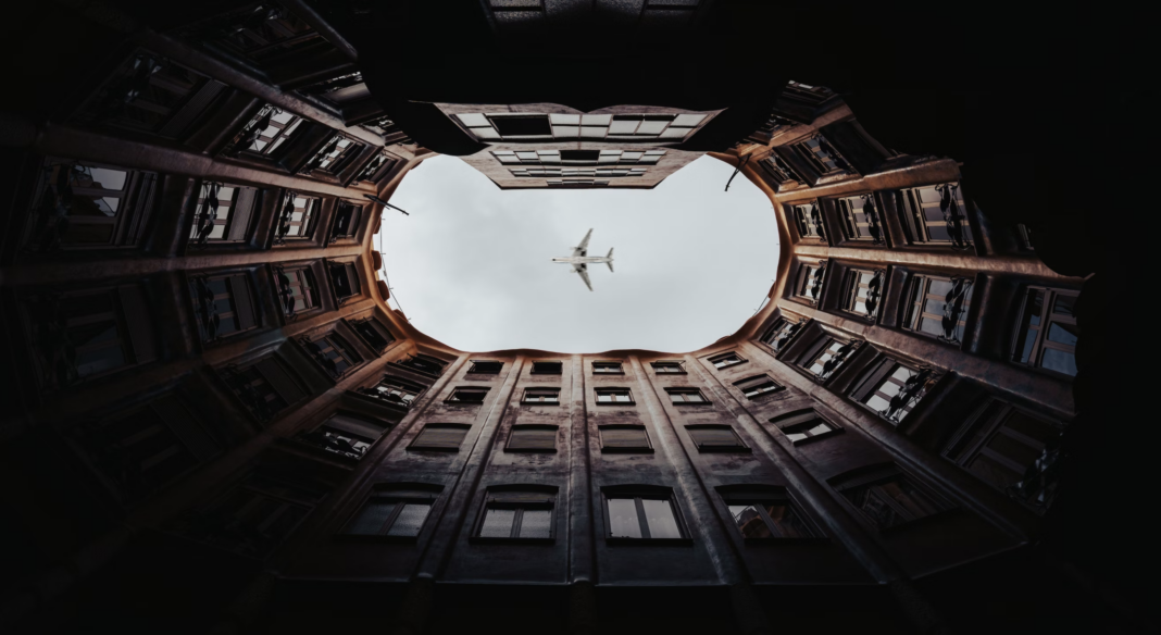 airplane flying over window of apartments